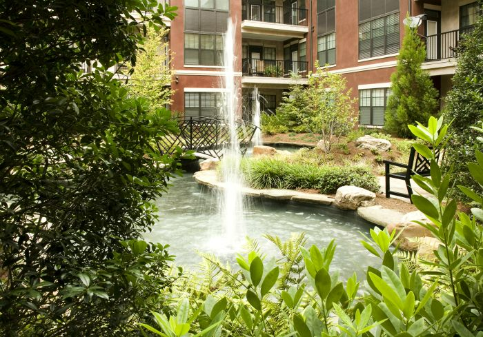 there is a fountain in the middle of a pond in front of a building .