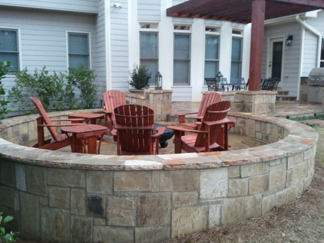 a fire pit with wooden chairs and tables in front of a house