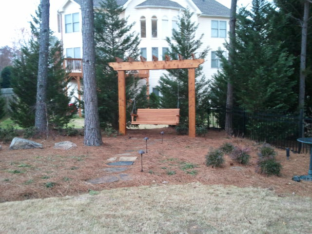 a wooden swing under a pergola in front of a house