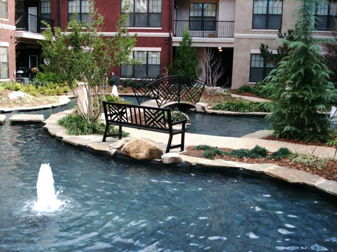 a pond with a fountain and a bench in the middle