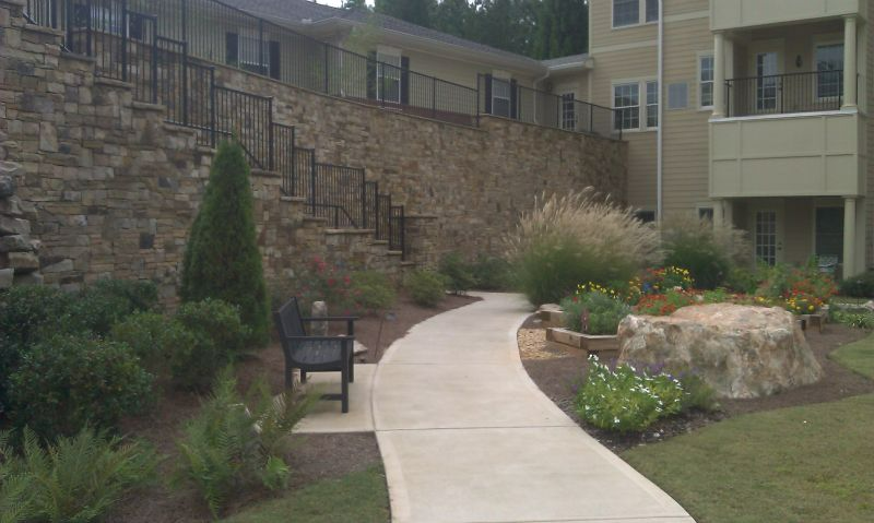 a concrete walkway leading to a building next to a stone wall .