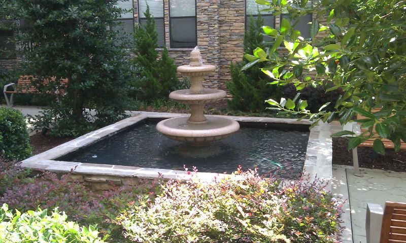 a fountain in a garden with a bench in the background.