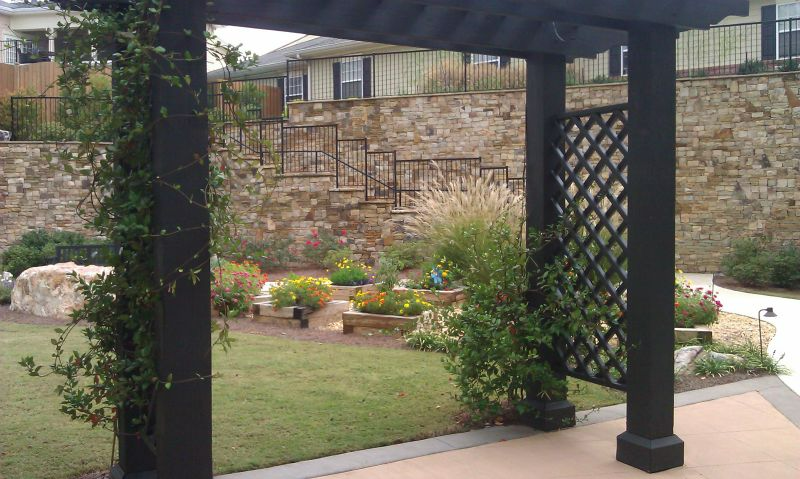 a pergola in a backyard with a stone wall in the background
