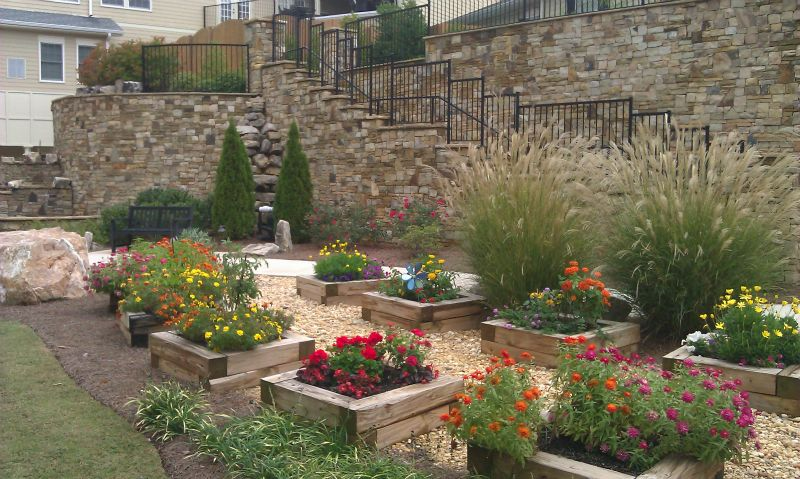 a garden filled with lots of flowers and plants in front of a stone wall .