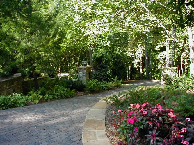 a brick driveway surrounded by trees and flowers.