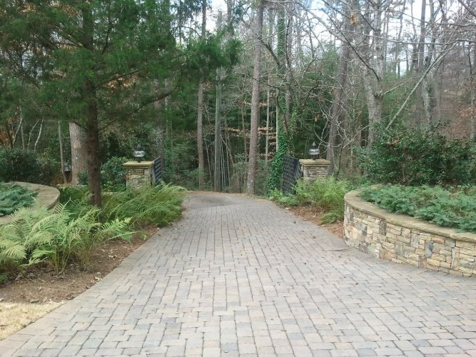 a brick driveway leading to a gate in the woods .