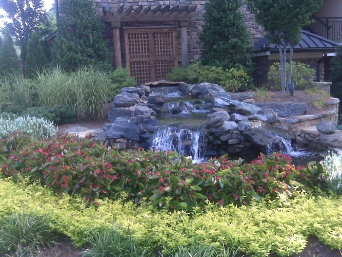 there is a waterfall in the middle of a garden surrounded by flowers .