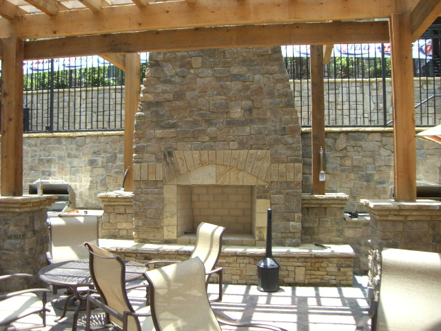 a stone fireplace sits under a wooden pergola