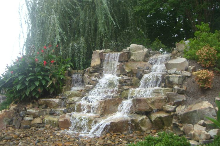 a waterfall is surrounded by rocks and trees in a garden .