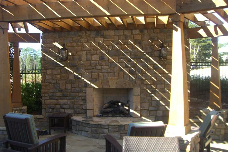 a patio with a fireplace and chairs under a pergola
