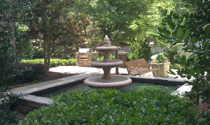 a fountain in a garden surrounded by trees and bushes