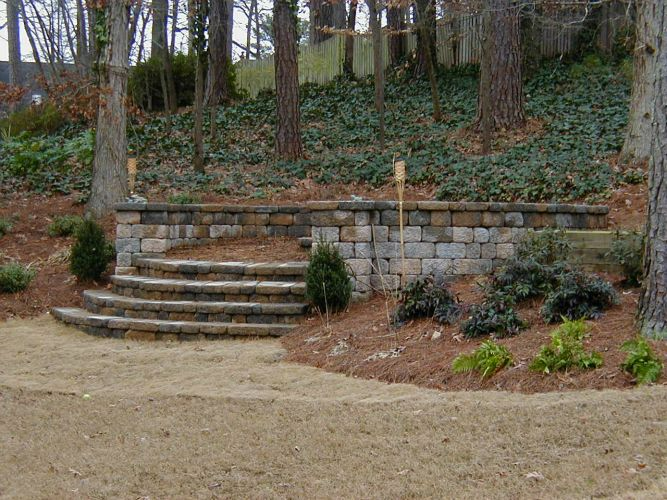 a stone wall with stairs leading up to it in the middle of a forest .