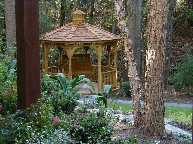 a wooden gazebo in the middle of a forest surrounded by trees .