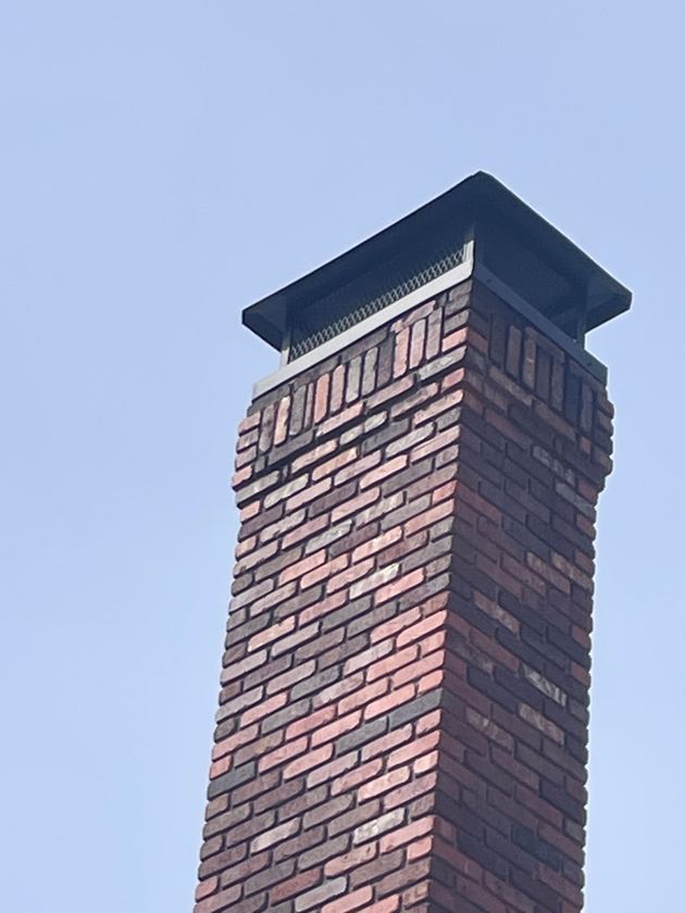 Brick chimney with a dark metal cap against a clear blue sky