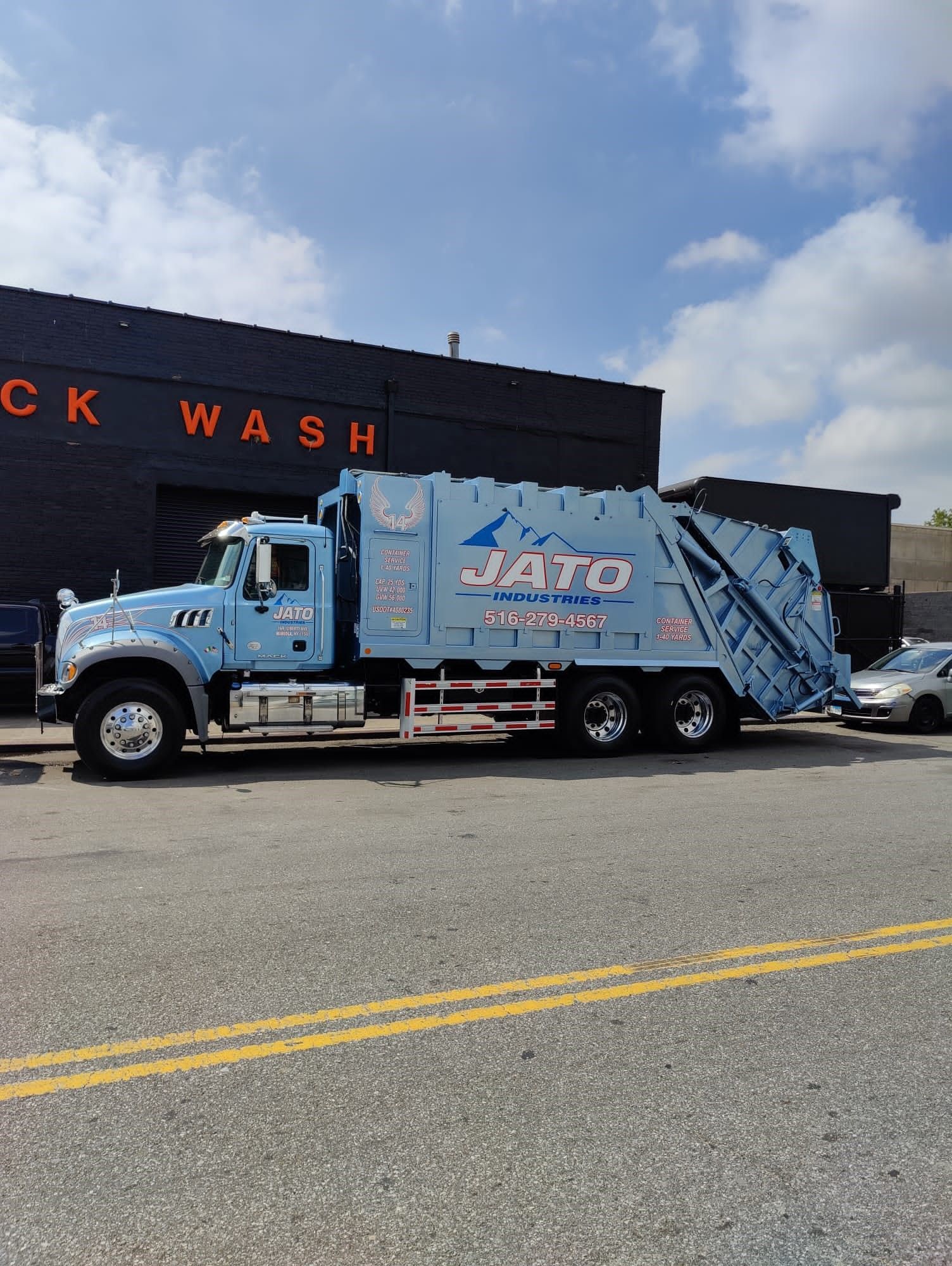 A blue garbage truck is parked in front of a truck wash
