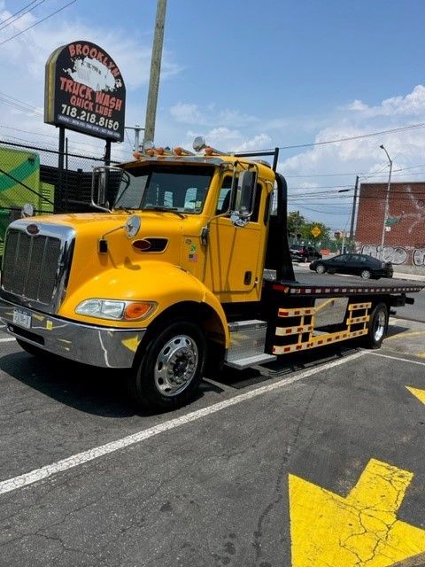 A yellow tow truck is parked in front of a truck wash