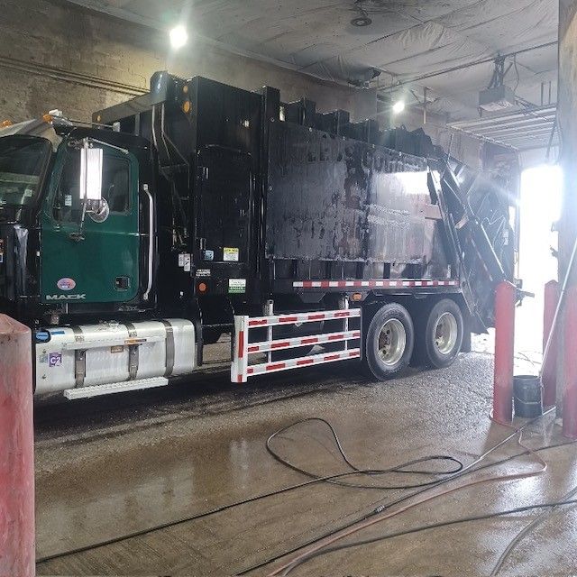 A black garbage truck is parked in a garage