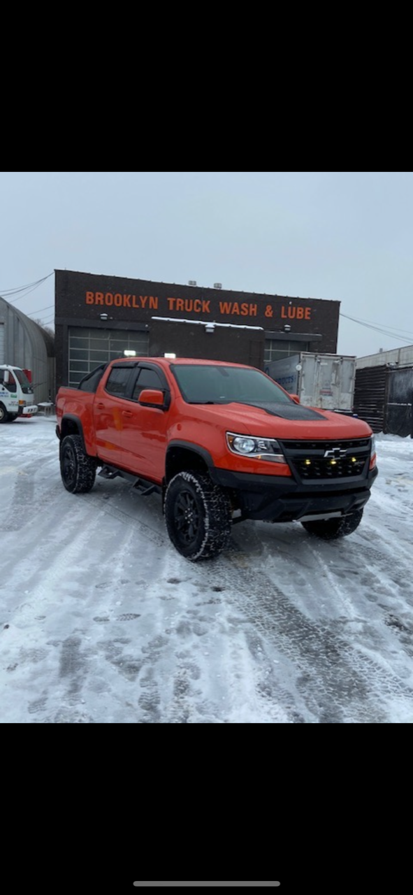 A red truck is parked in the snow in front of a building
