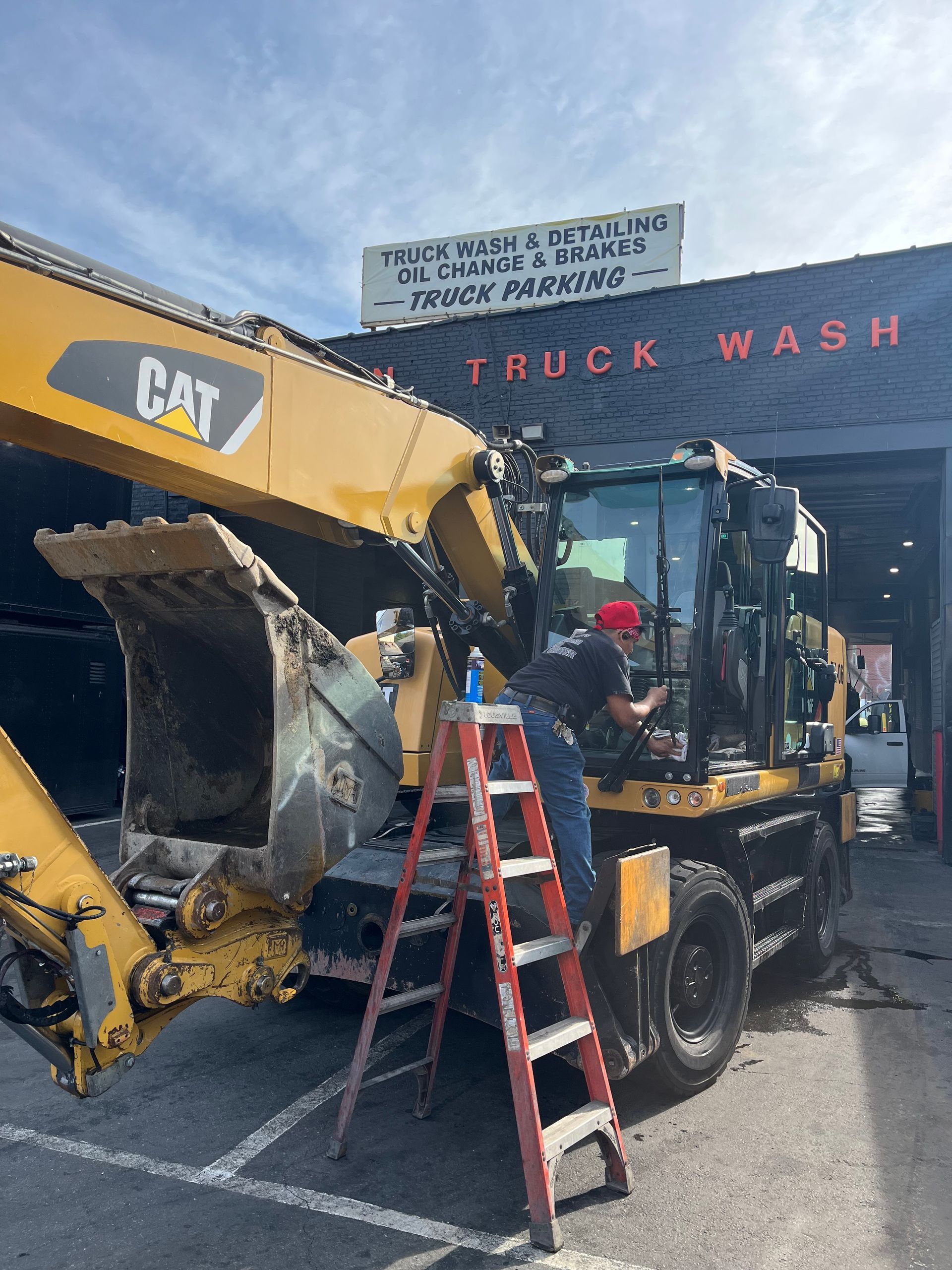 A man is cleaning a CAT excavator in front of a truck wash