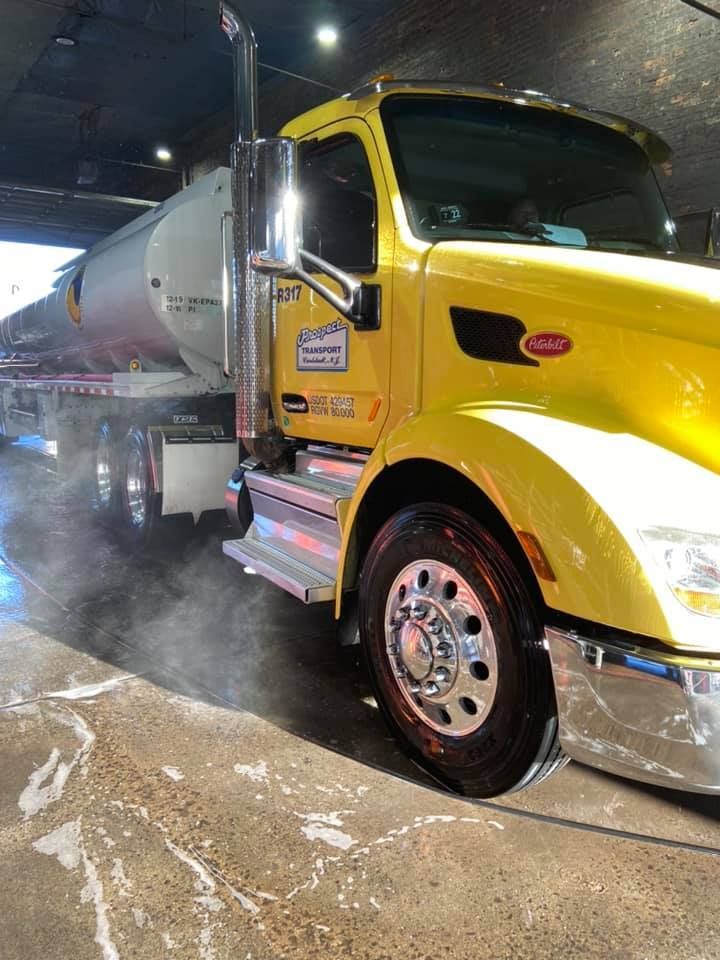 A yellow truck with a white tank on the back is being cleaned