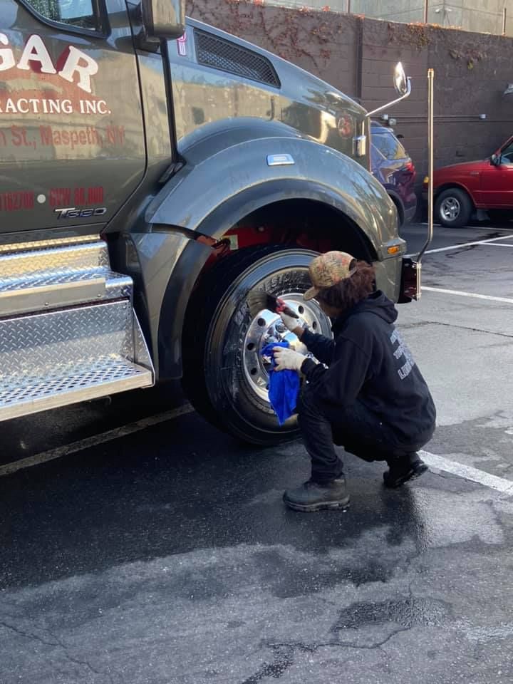 A man is crouched while cleaning a truck tire