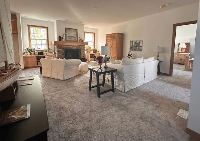 Spacious living room with gray carpet, white sofas, fireplace, and sunlight through windows