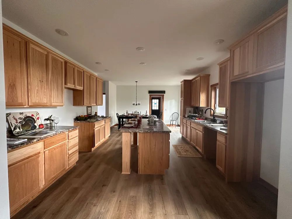 Long kitchen with wood cabinets, island, dark countertops, and a window at the far end.
