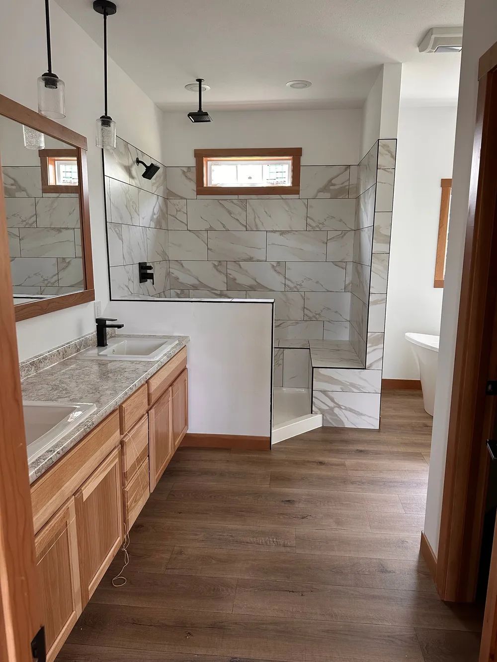 Modern bathroom with wood vanity, granite countertop, and tiled walk-in shower under small windows