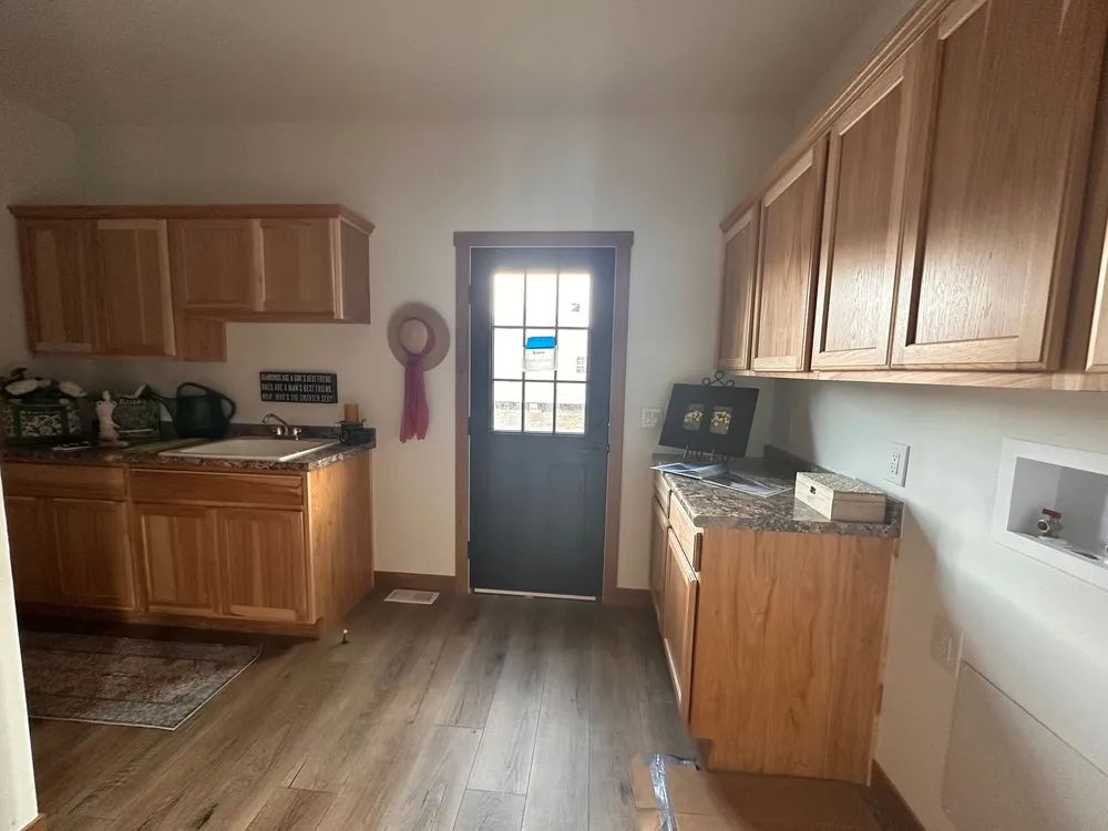 Kitchen with wood cabinets, black door, and wood-look floor, viewed from the dining area.