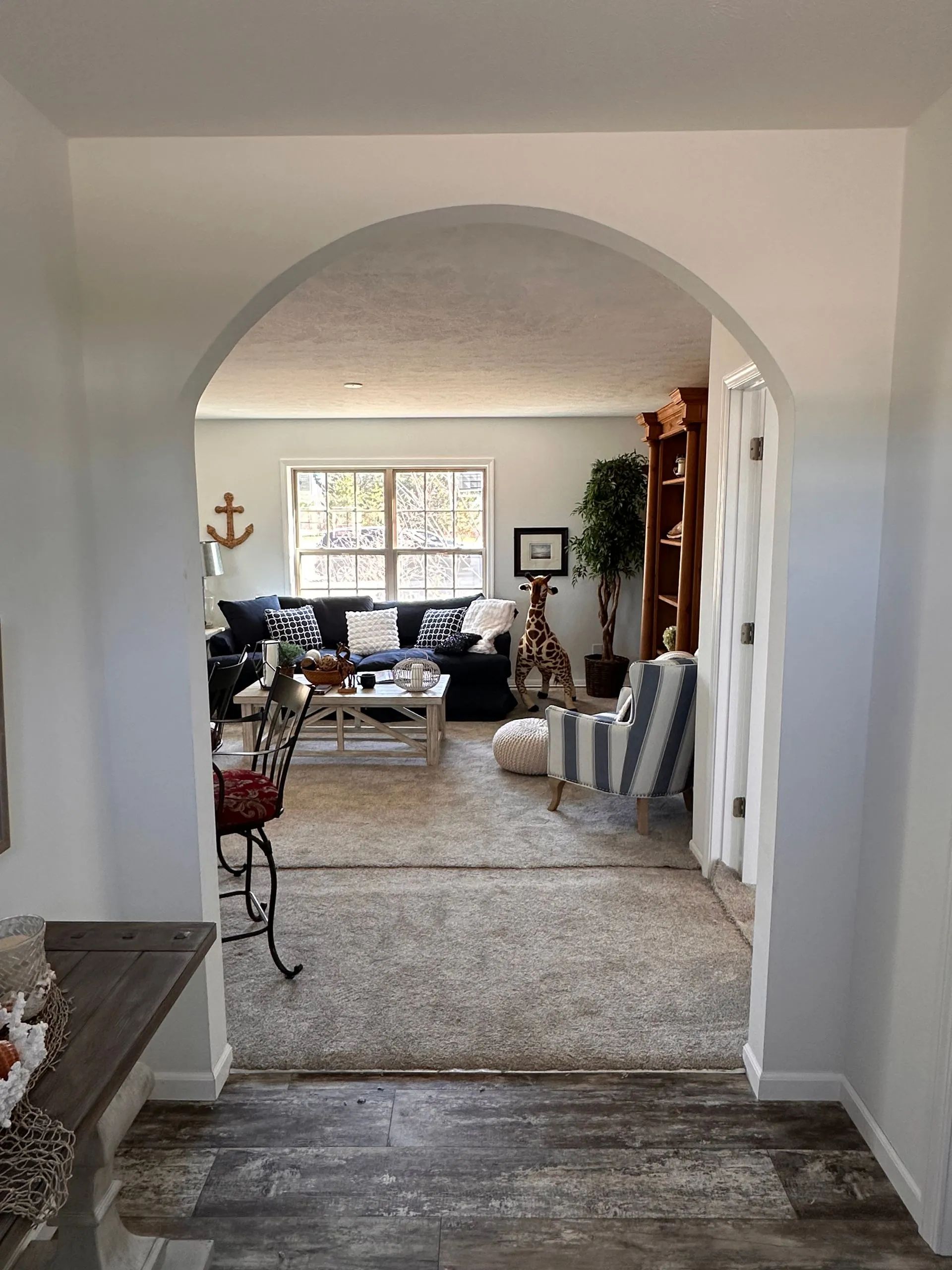 Archway view into a cozy living room with a sofa, striped chair, window, and plants