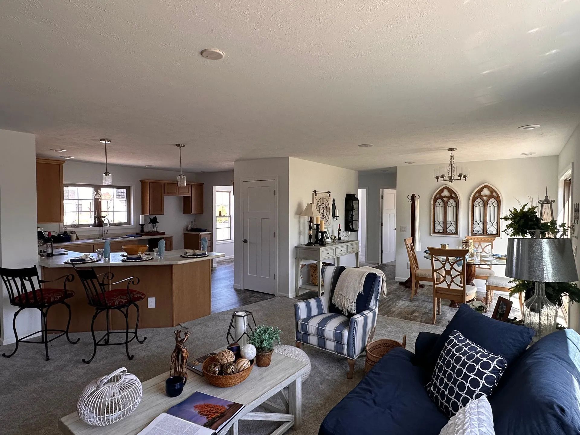 Open-concept living room with blue sofa, coffee table, dining area, and kitchen in the background