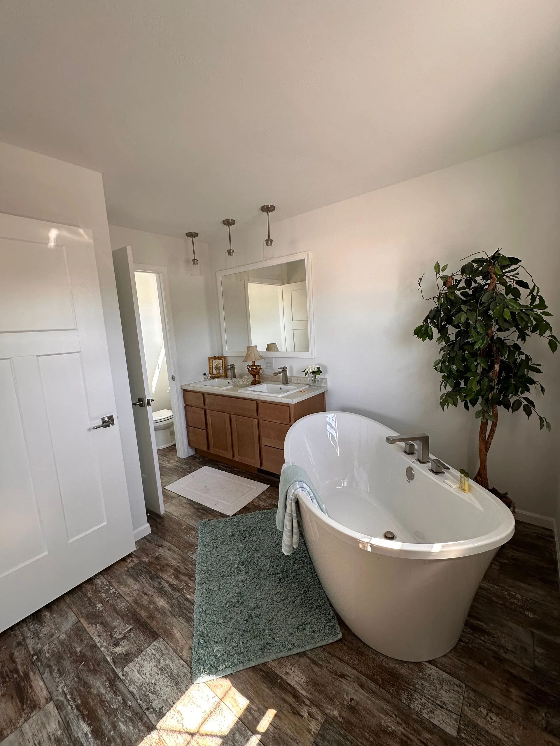 Bright bathroom with freestanding tub, wood vanity, large mirror, and green rug
