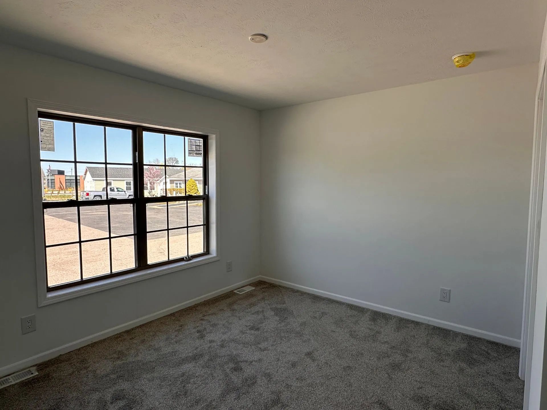 Empty carpeted bedroom with large window and white walls, shown in daylight