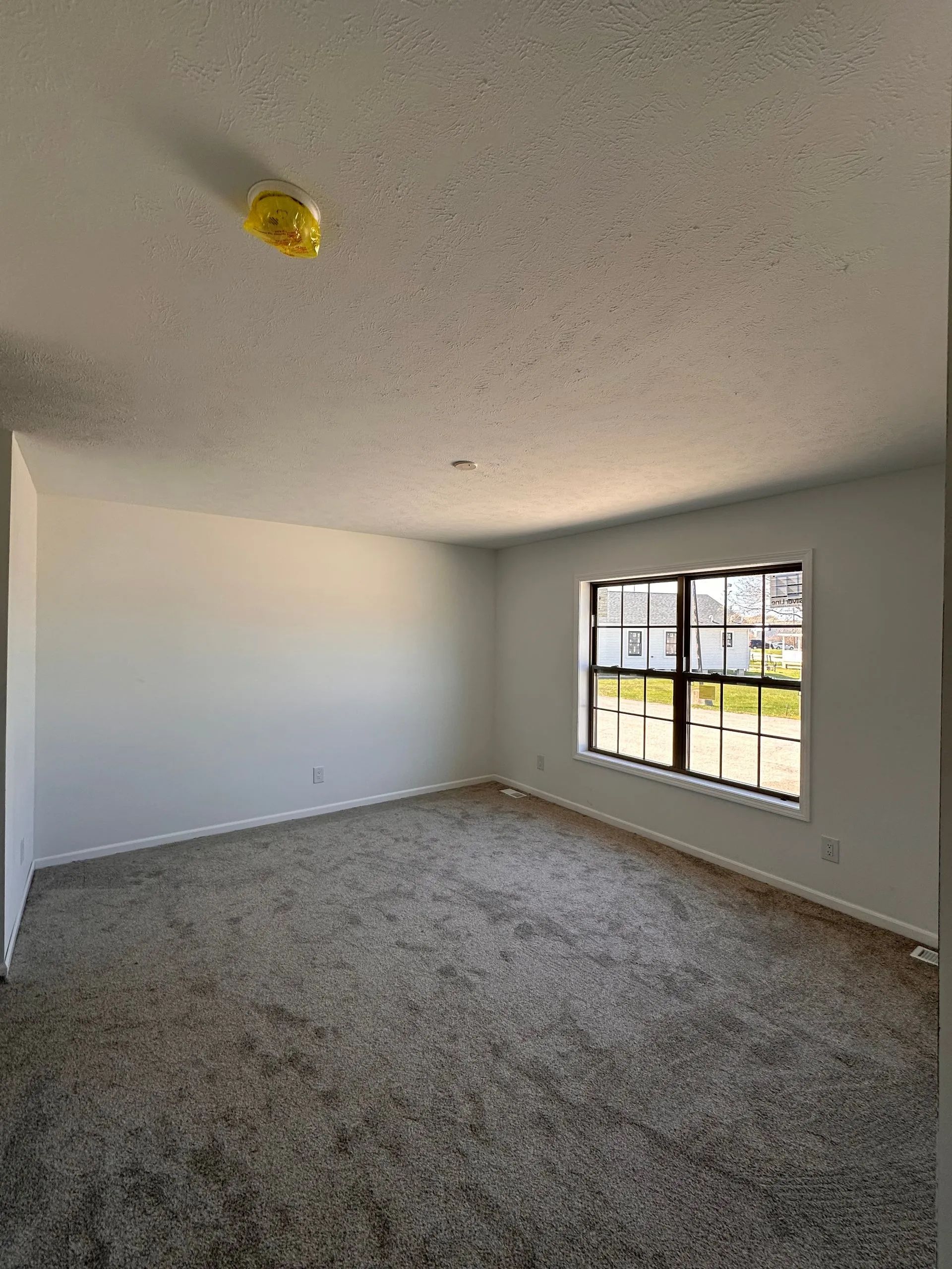 Empty carpeted room with white walls and a window letting in daylight.