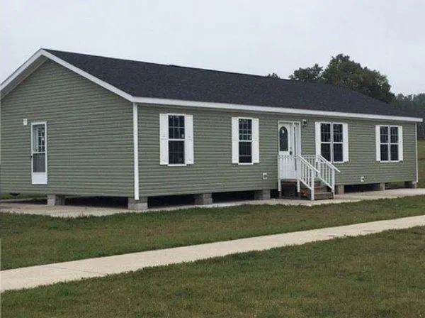 Single-story green house with white trim, front porch steps, and a sloped dark roof.