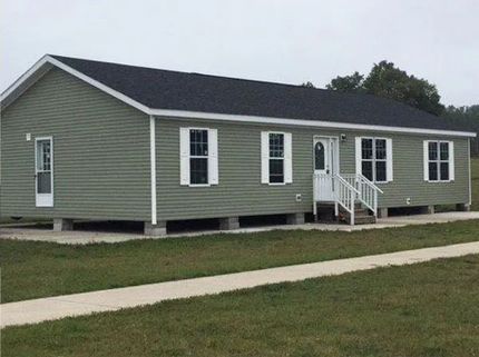 Single-story green house with white trim, front porch steps, and a sloped dark roof.