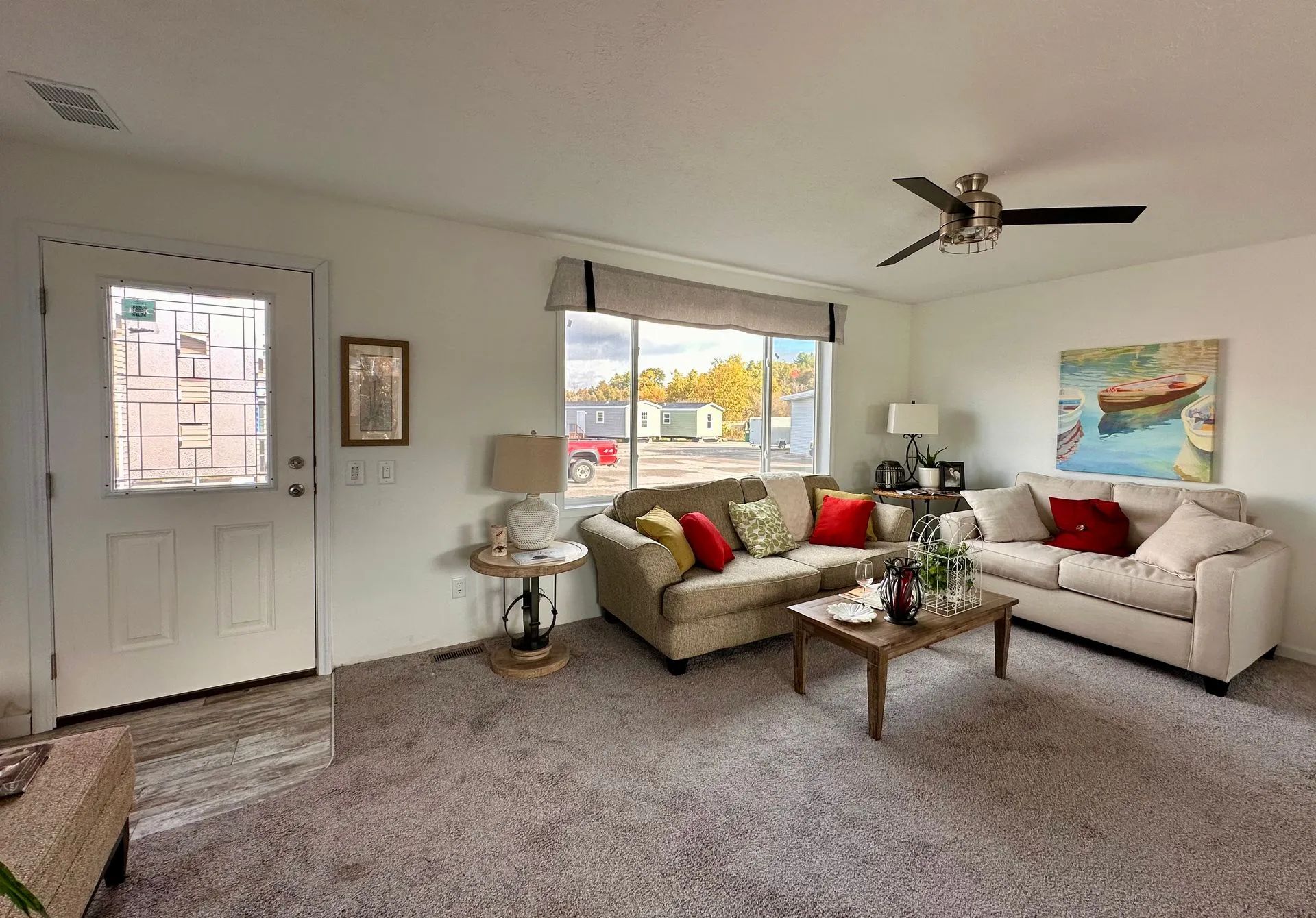 Bright living room with beige sofas, red pillows, coffee table, and large window.