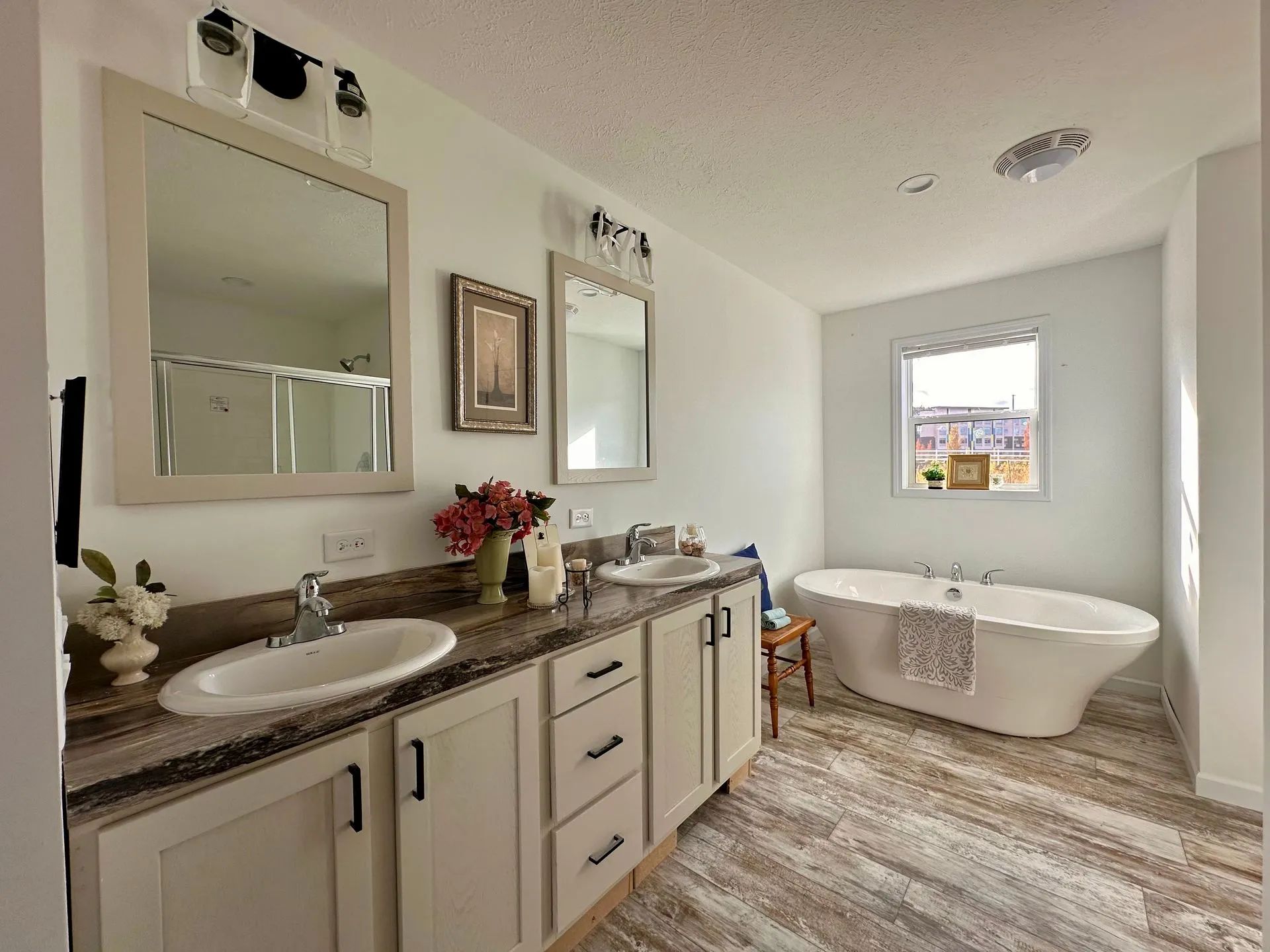 Bright bathroom with double vanity, large mirrors, and a freestanding tub by the window.