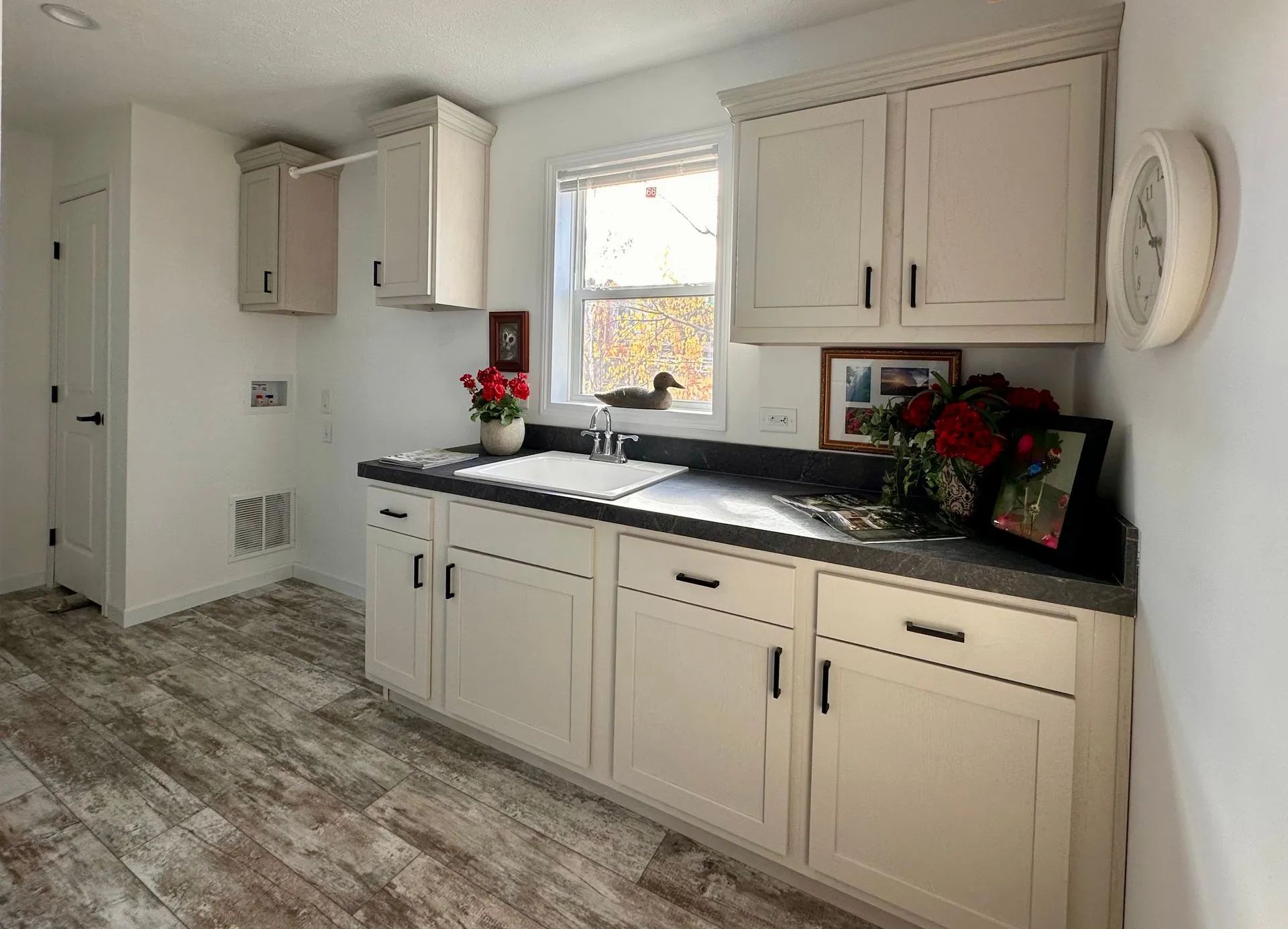 Bright white kitchen with cream cabinets, dark counters, gray tile floor, and a window over the sink.
