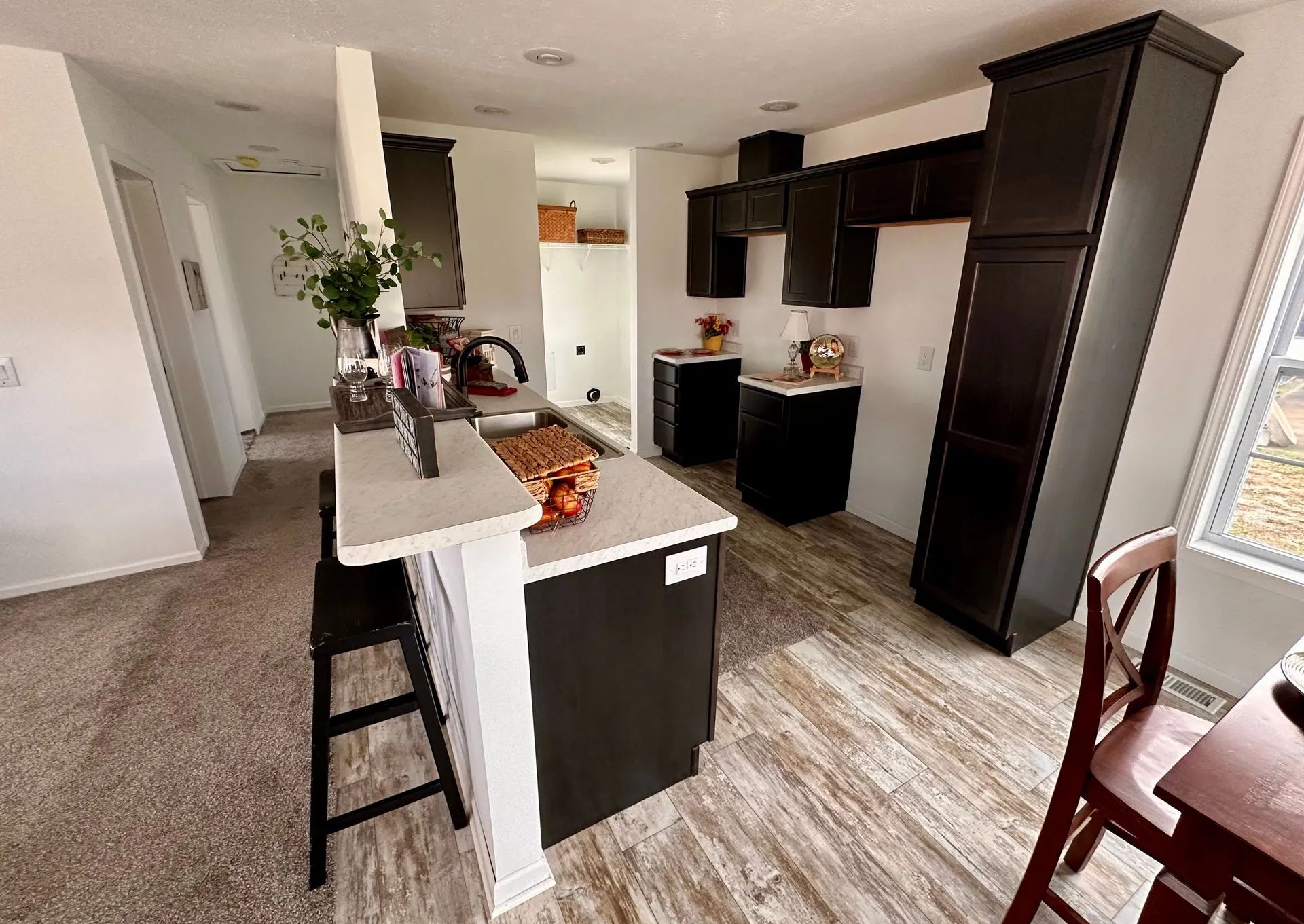 Modern kitchen with dark cabinets, white island, and dining chairs near a windowed wall.