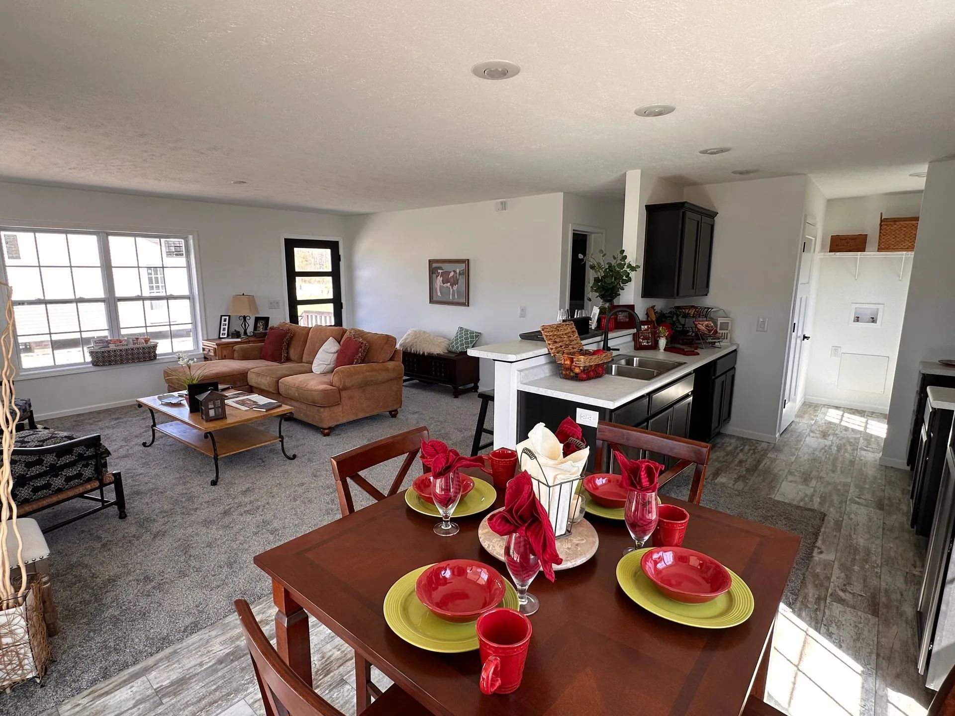 Open-concept dining and living room with red table settings, brown furniture, and large windows
