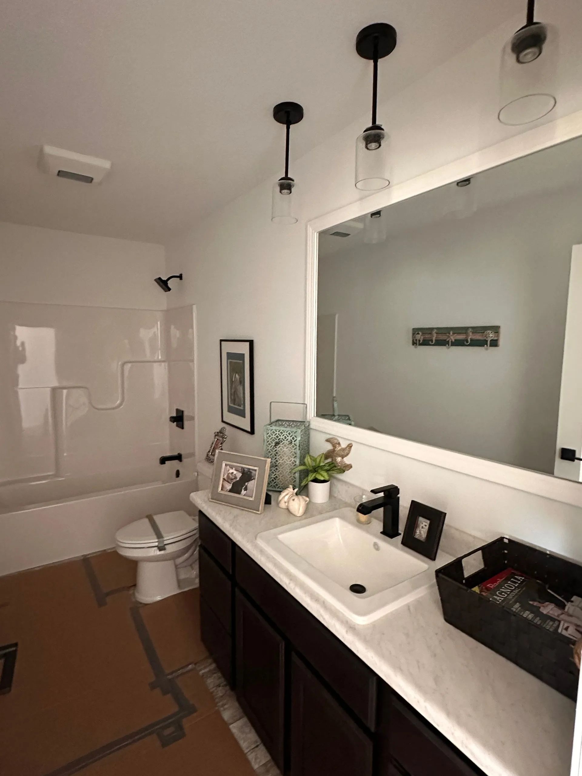 Modern bathroom with white walls, dark vanity, sink, large mirror, toilet, and black pendant lights