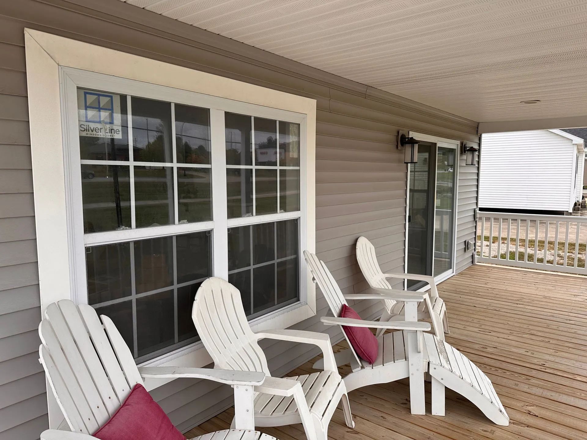 Covered porch with white chairs and small table beside sliding glass doors and gray siding
