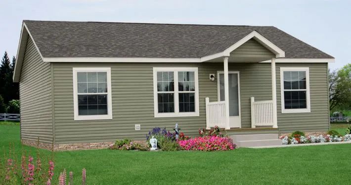 Single-story beige house with white trim, front porch, and flower bed on a green lawn