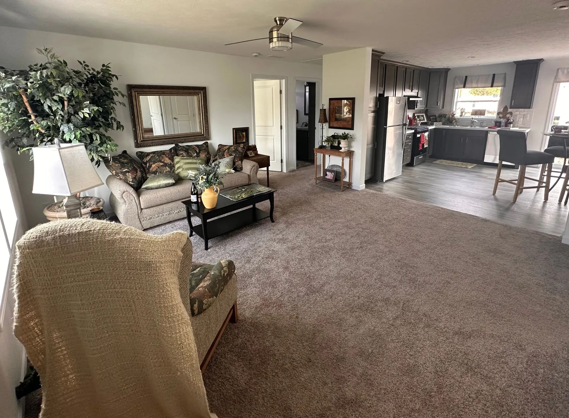 Spacious living room with gray seating, fireplace, large mirror, and open view into a kitchen area