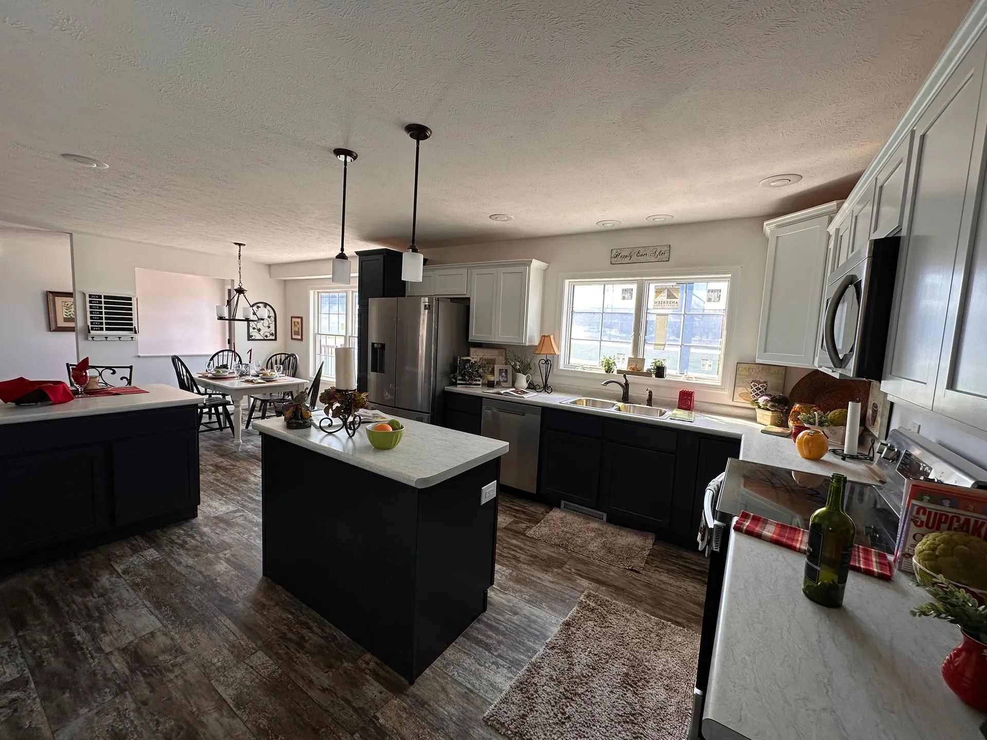 Bright kitchen with black cabinets, island, stainless fridge, and pendant lights in an open layout