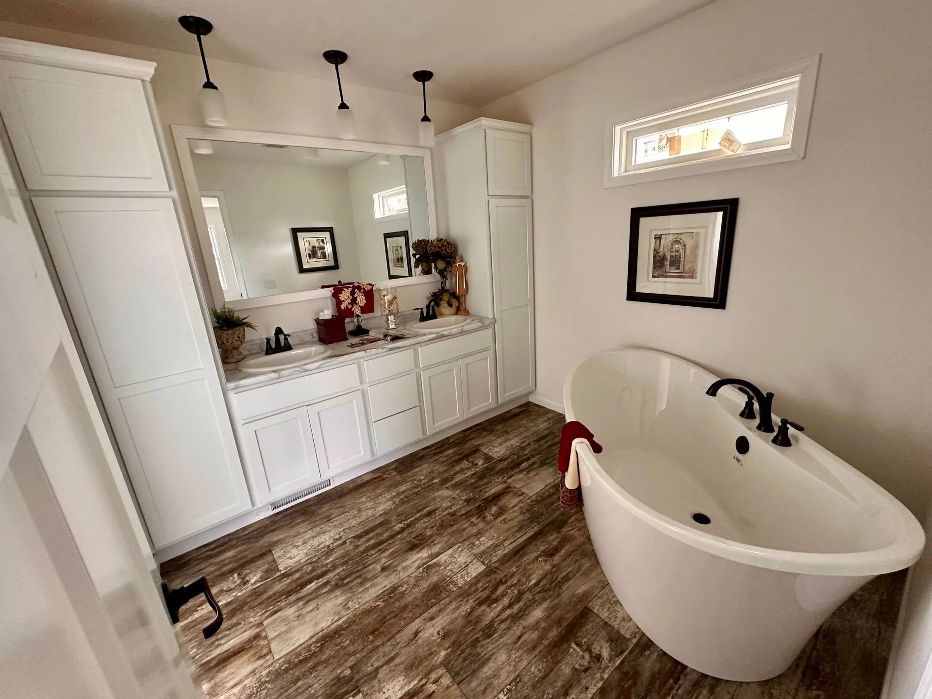 Bright bathroom with white vanity, large mirror, wood-look floor, and a freestanding tub by the wall.