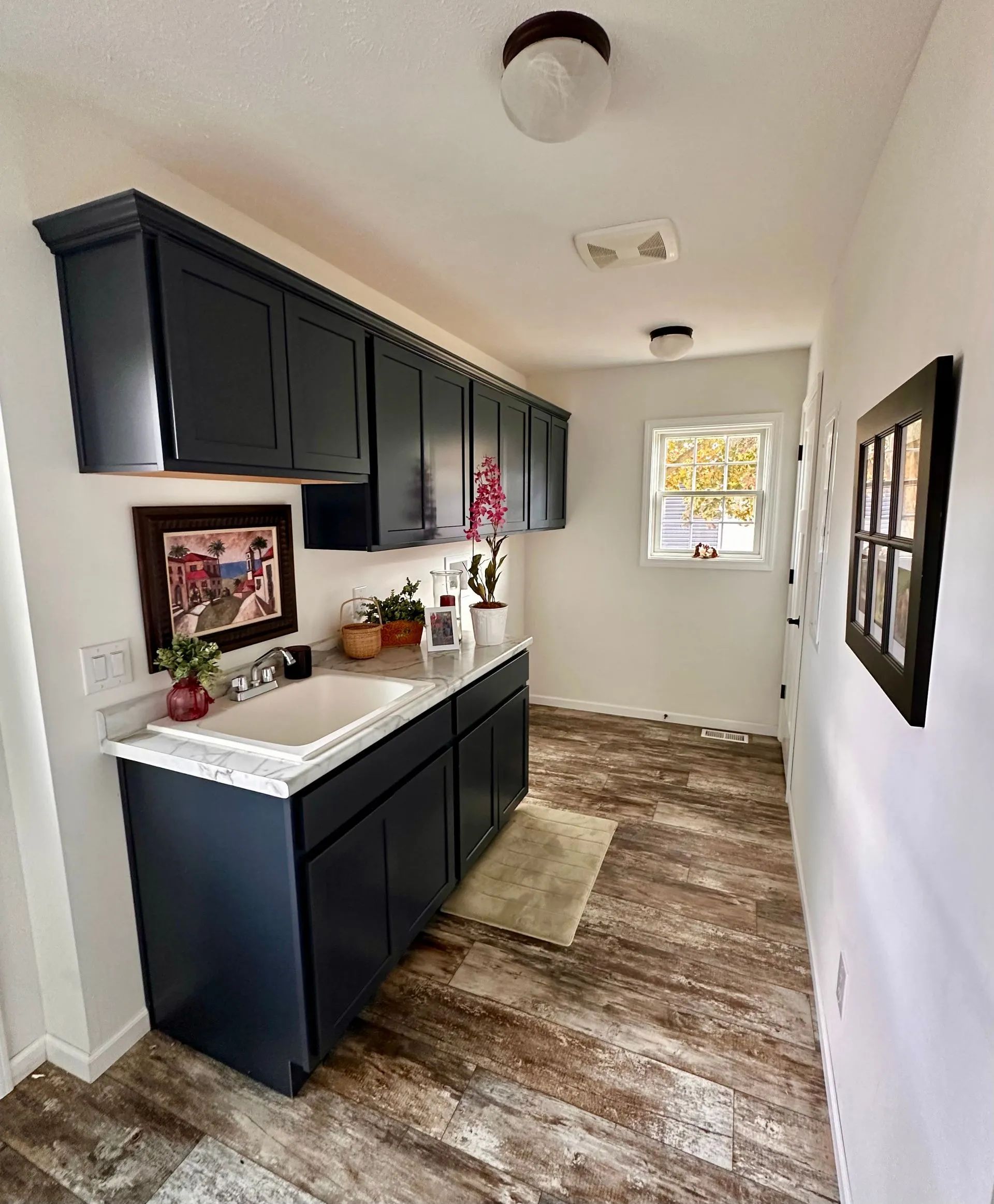 Narrow kitchen with dark cabinets, white countertops, and worn wood flooring