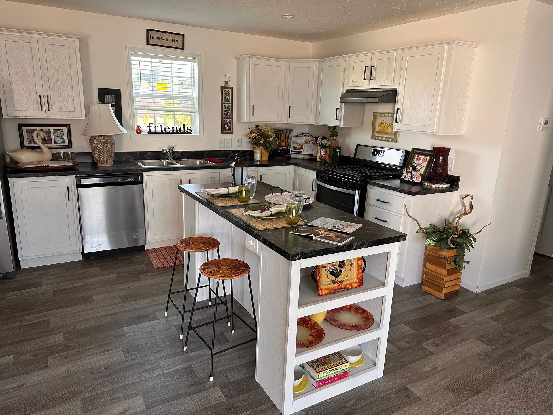 Bright modern kitchen with white cabinets, black countertops, island, stainless appliances, and gray wood flooring