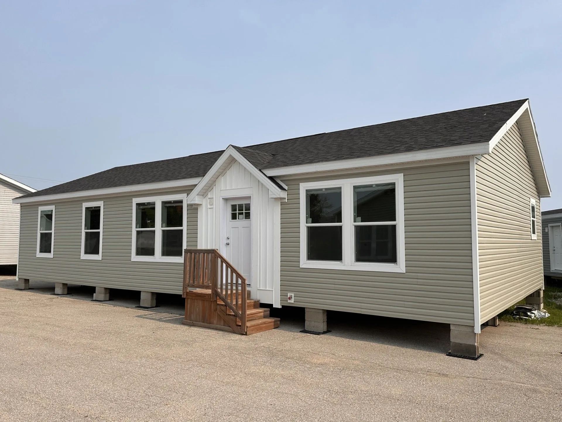 Single-story beige modular home with white trim and a small front porch on a gravel lot